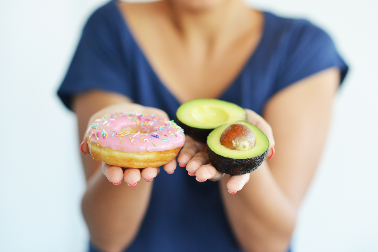 Woman holding a donut and two halves of avocado - showing the best and worst foods to take when you have Ulcerative Colitis.