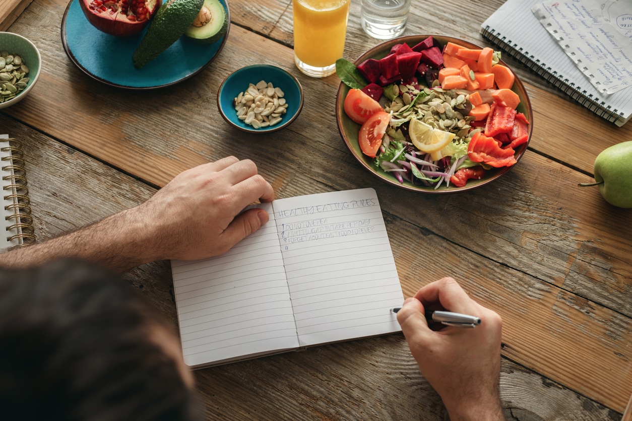 Man writing different recipes on his notebook - creating a list of healthy foods to manage his IBD. And writing crohn's disease diet recipes out.