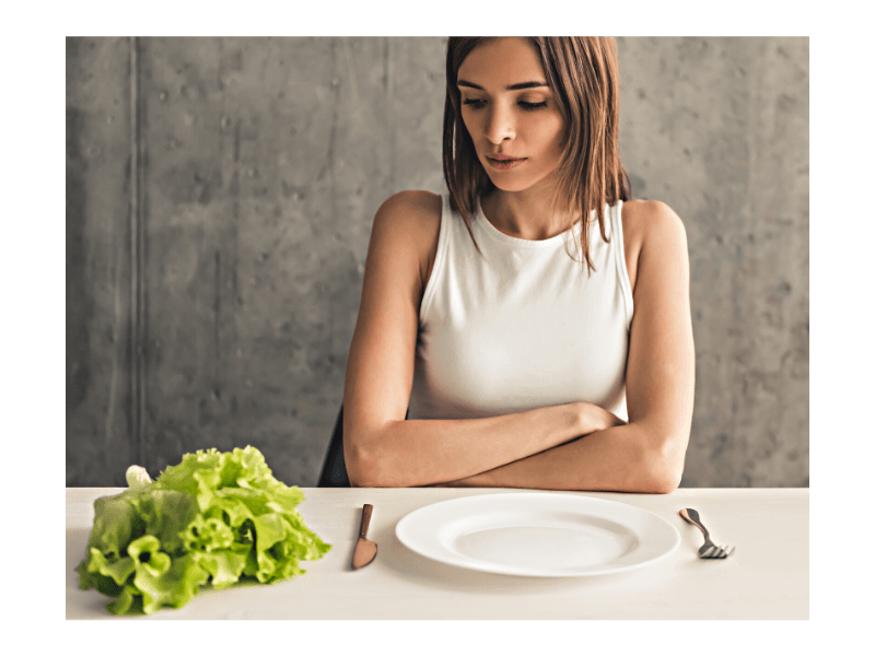 woman sitting at table with empty plate struggling with disordered eating