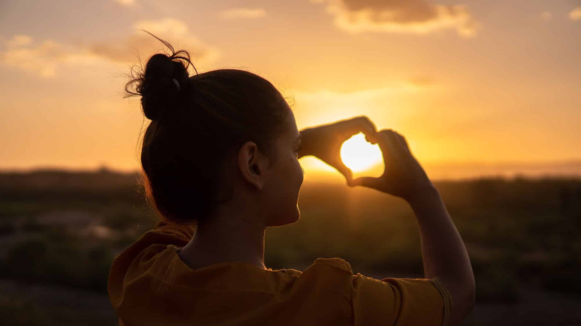 Silhouette of a woman holding up hands into a sunset and makes a heart, Crohn's and Colitis Dietitians