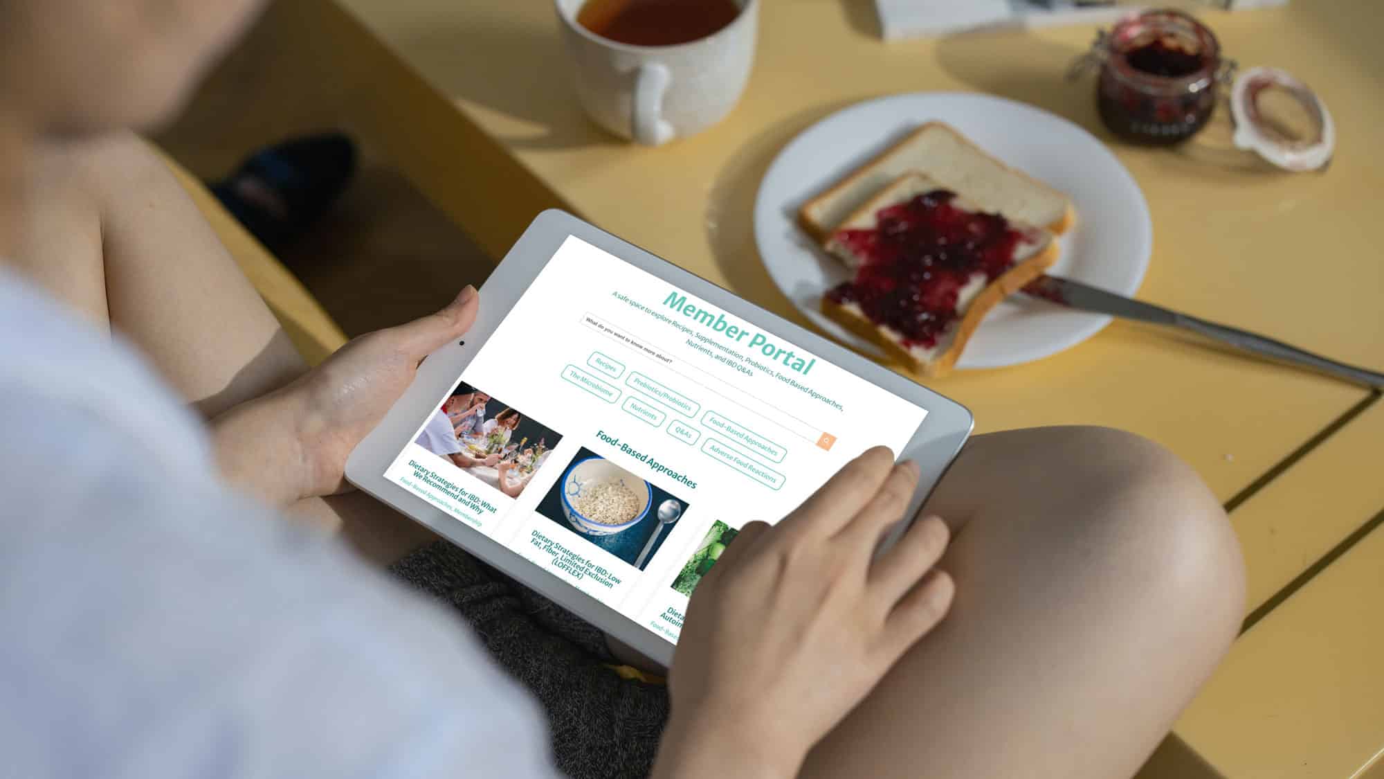 iPad screen showing IBD member portal in the hands of woman eating breakfast