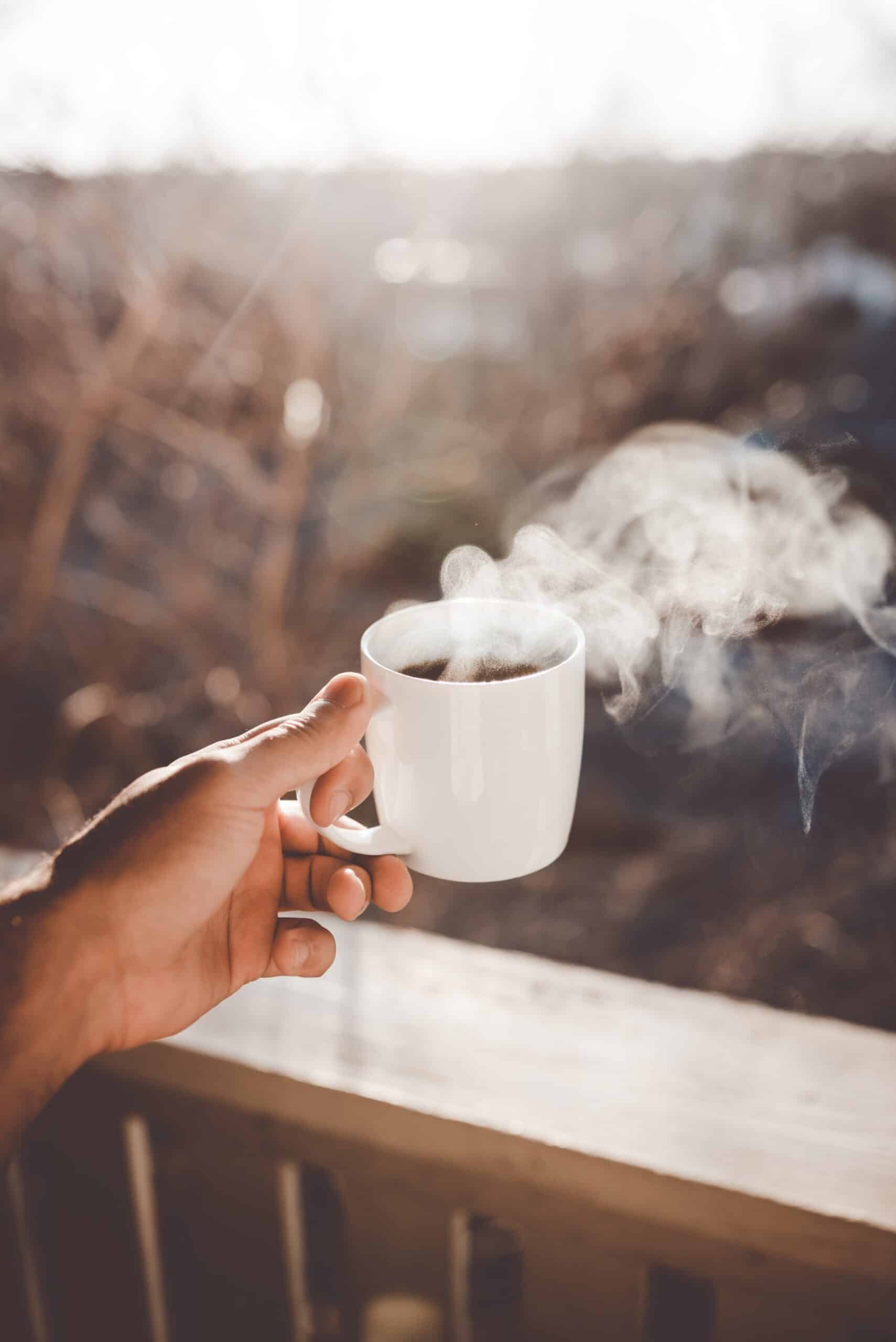 Coffee and Ulcerative Colitis - do they belong together? A hand holding a cup of steaming coffee on a deck