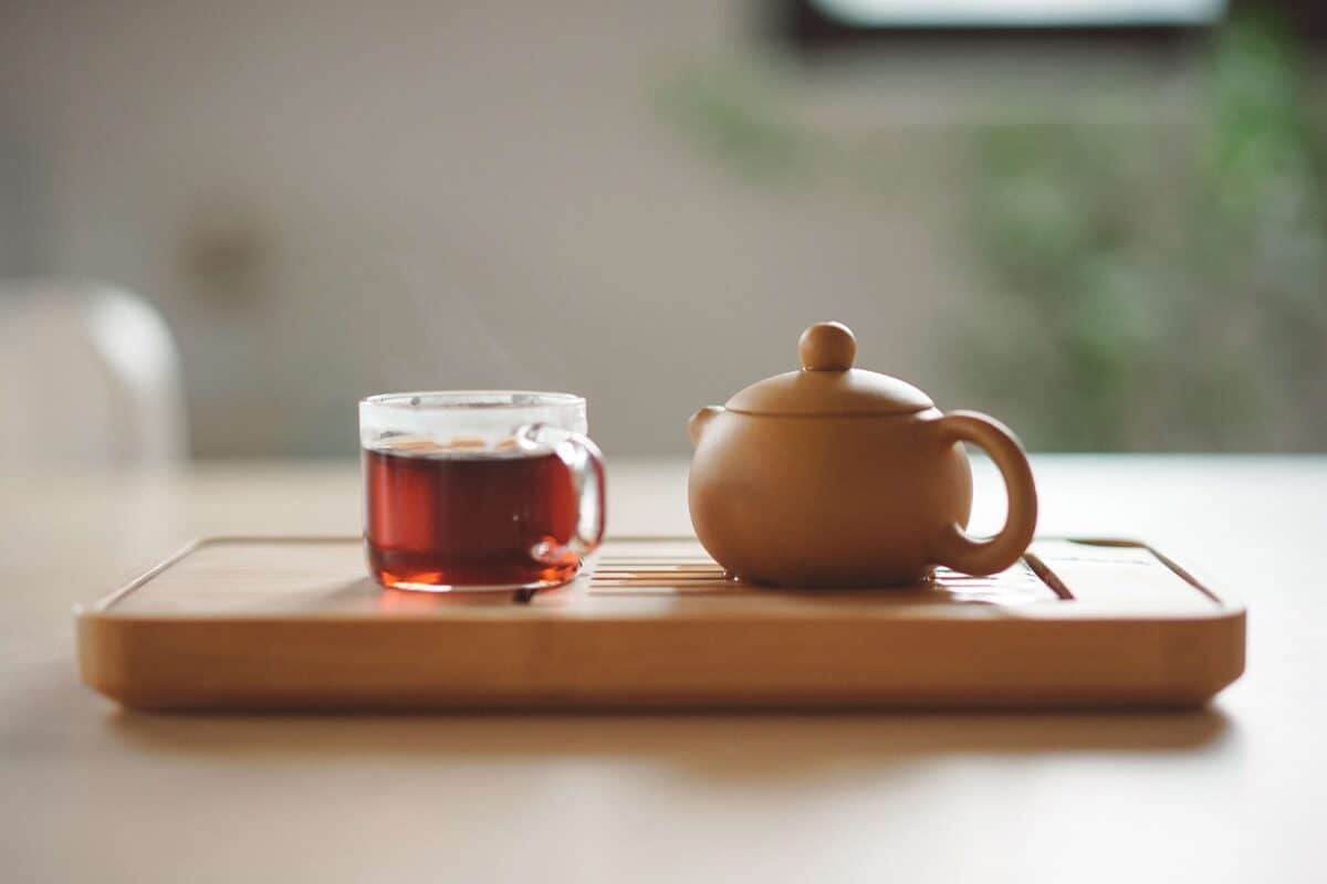 A teapot and cup of herbal tea placed on a wooden board.